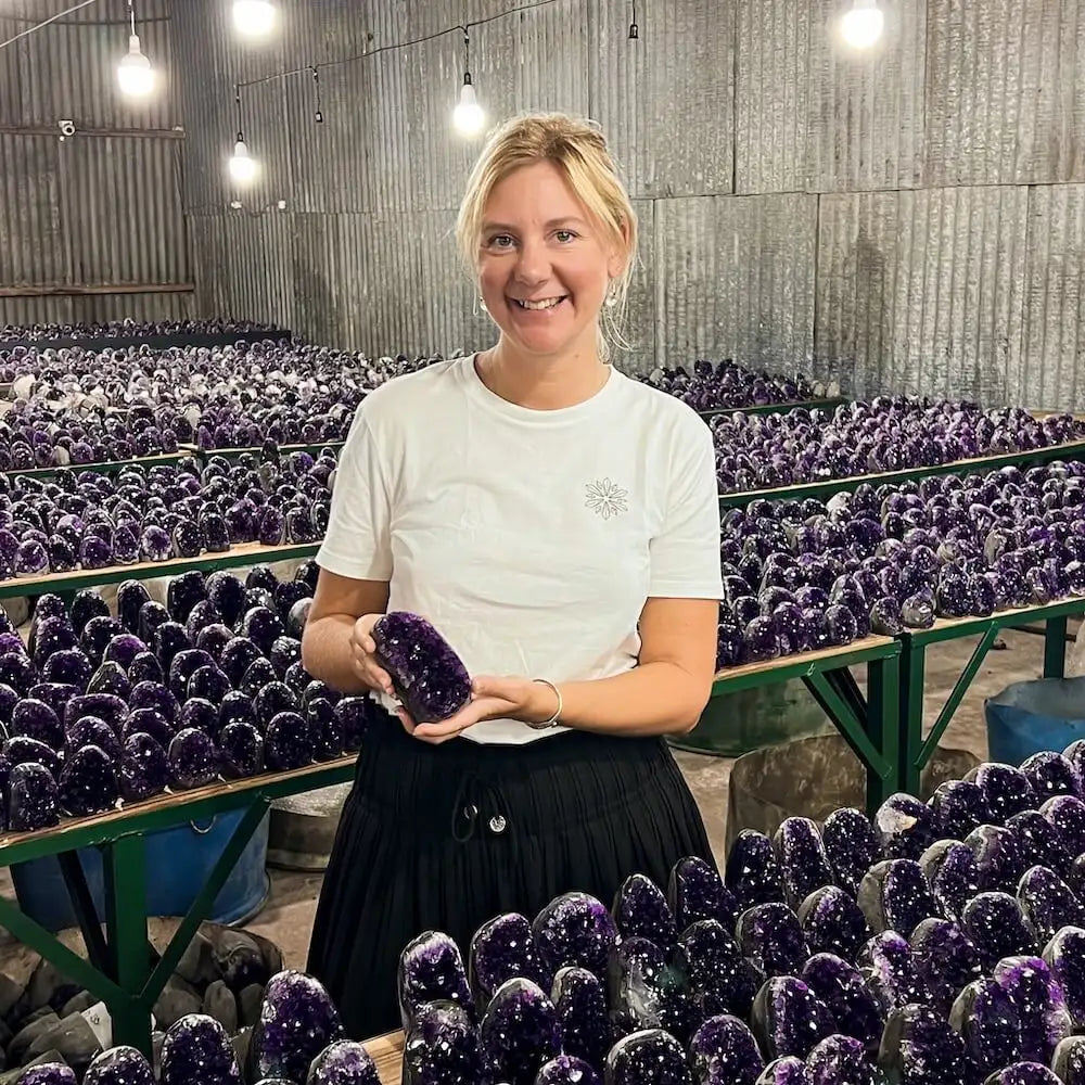 Une femme tient une géode d'améthyste violette polie avec des facettes de cristaux blancs scintillants.
