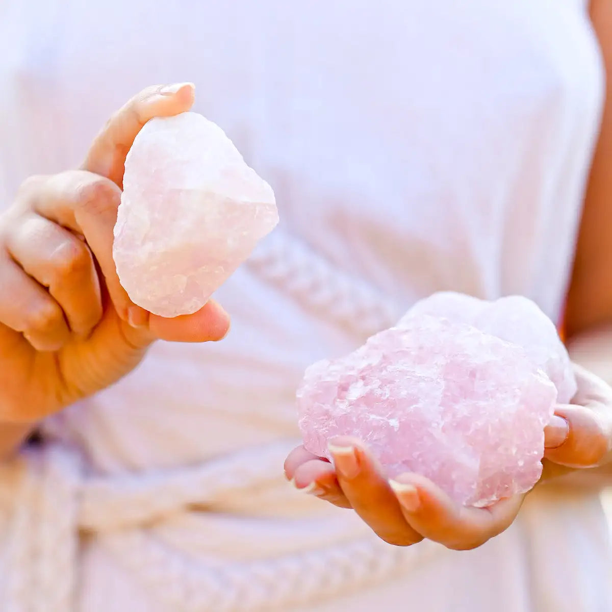 Deux morceaux de quartz rose brut, un lisse et rose pâle dans la main gauche, un autre plus rugueux avec une teinte rose plus vive tenu dans la main droite.